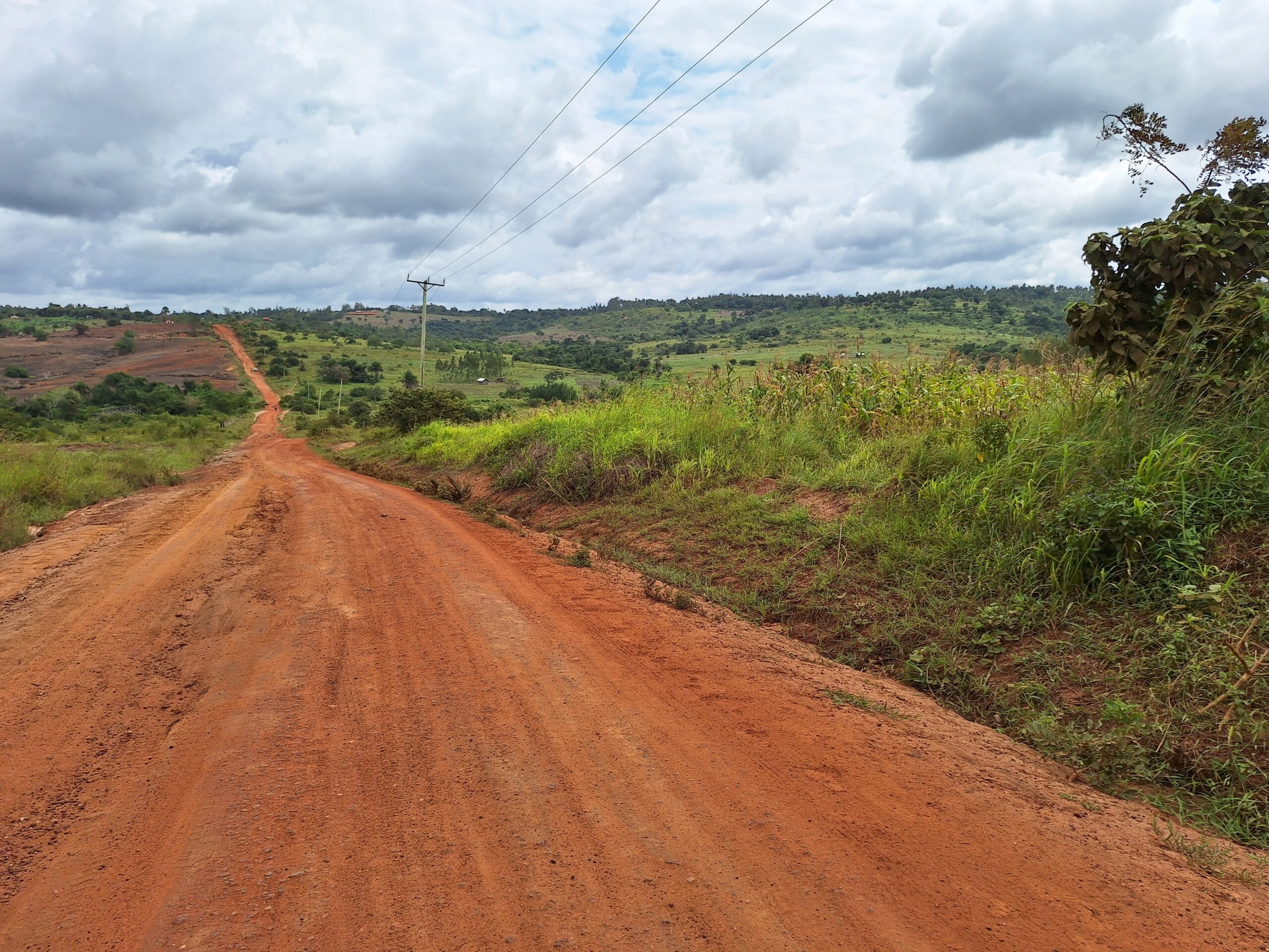 Landschap met bewolkte lucht, groen en rood zand als weg in Kenia